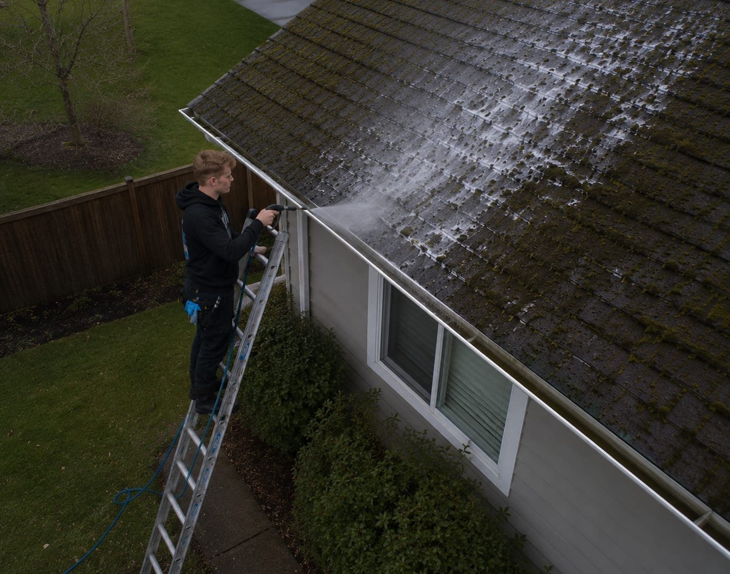 Ethan Olson soft-washing a mossy roof from a ladder